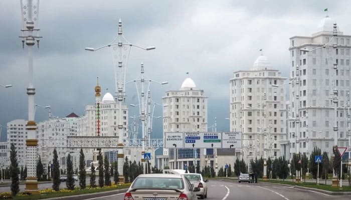 imagem de carros percorrendo uma larga avenida em Ashgabat; ao fundo podemos ver enormes edifícios de mármore branco
