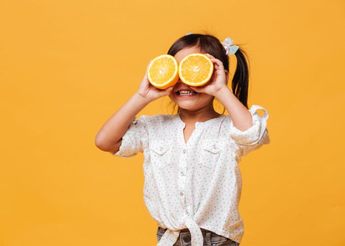 menina criança cobrindo os olhos com laranja
