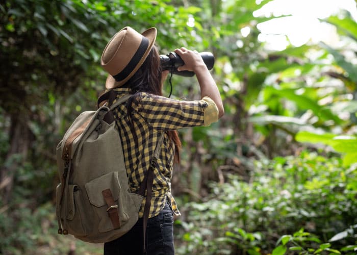 mulher jovem com mochila nas costas olhando ao binóculo na selva