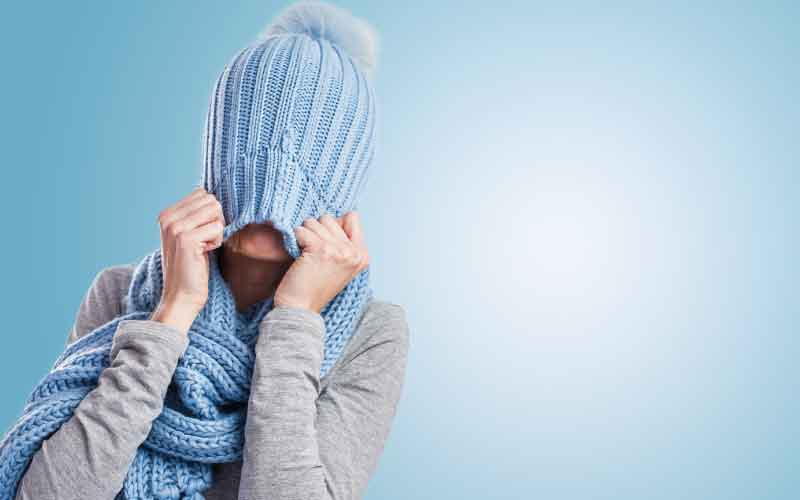 Mulher puxando a toca de forma a cobrir o rosto, representando o clima frio